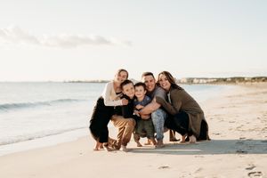 A group of loved ones crouch together with their dog for a sunset portrait on a pristine beach.
