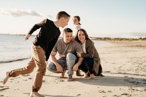 A couple sits playfully together on a sandy beach during an intimate outdoor photoshoot.