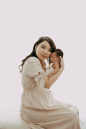 A gentle moment captured between parent and infant in soft beige tones against a minimal white background.