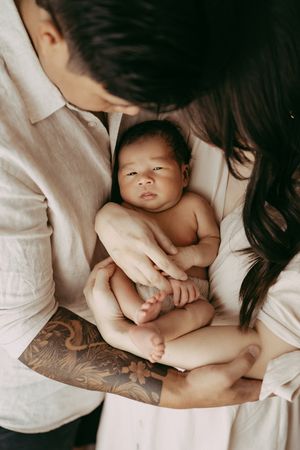 A precious newborn baby rests in the arms of parents, with one showing a detailed arm tattoo sleeve.