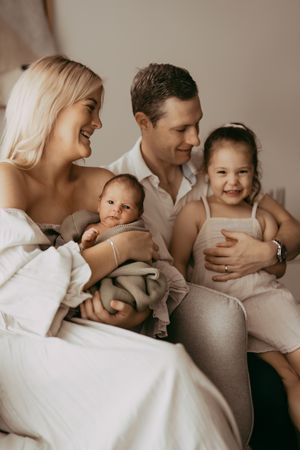 A family portrait in warm tones showing intimate moments between parents and their baby and toddler in white outfits.