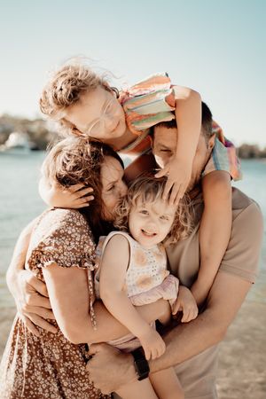 A family shares tender embraces and playful moments together on a sunny beach in natural sunlight.