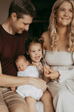 A family portrait showing parents with their children, including a toddler and newborn, all sitting together indoors.