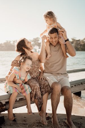 Happy family enjoying a sunny day together at the beach sitting on a wooden dock during golden hour.