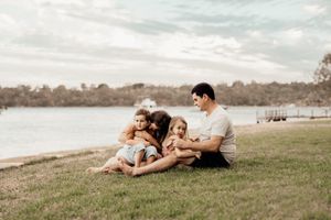 A romantic couple lying together on grassy hill overlooking lake during sunset in warm natural lighting.