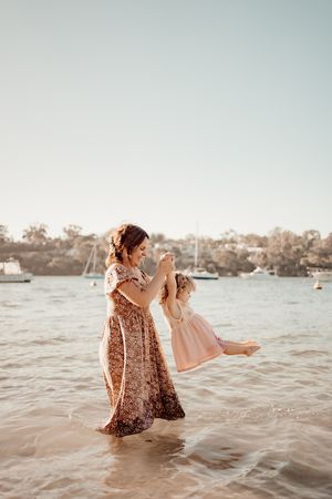 A couple shares a romantic moment standing in shallow water during sunset at a harbor with boats in the background.