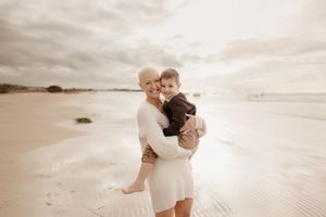 A romantic couple embraces on a serene beach during golden hour with cloudy skies and sandy shores in the background.