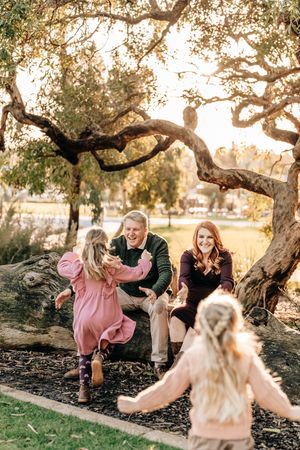 A playful outdoor photoshoot with a young family sitting and posing near a large twisted tree at golden hour.