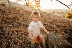 Young child sitting on a fallen log during golden hour in a nature setting.