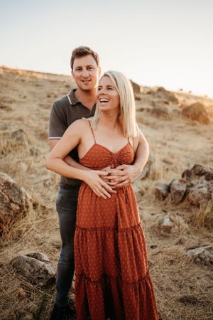 Couple sharing a joyful embrace on a golden hillside during sunset.