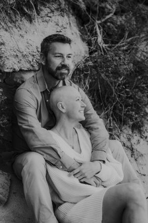 Black and white intimate portrait of couple resting against rock wall outdoors.