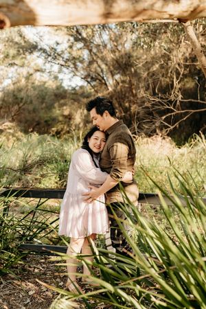 A couple shares an intimate moment together among tropical plants in a natural outdoor setting.