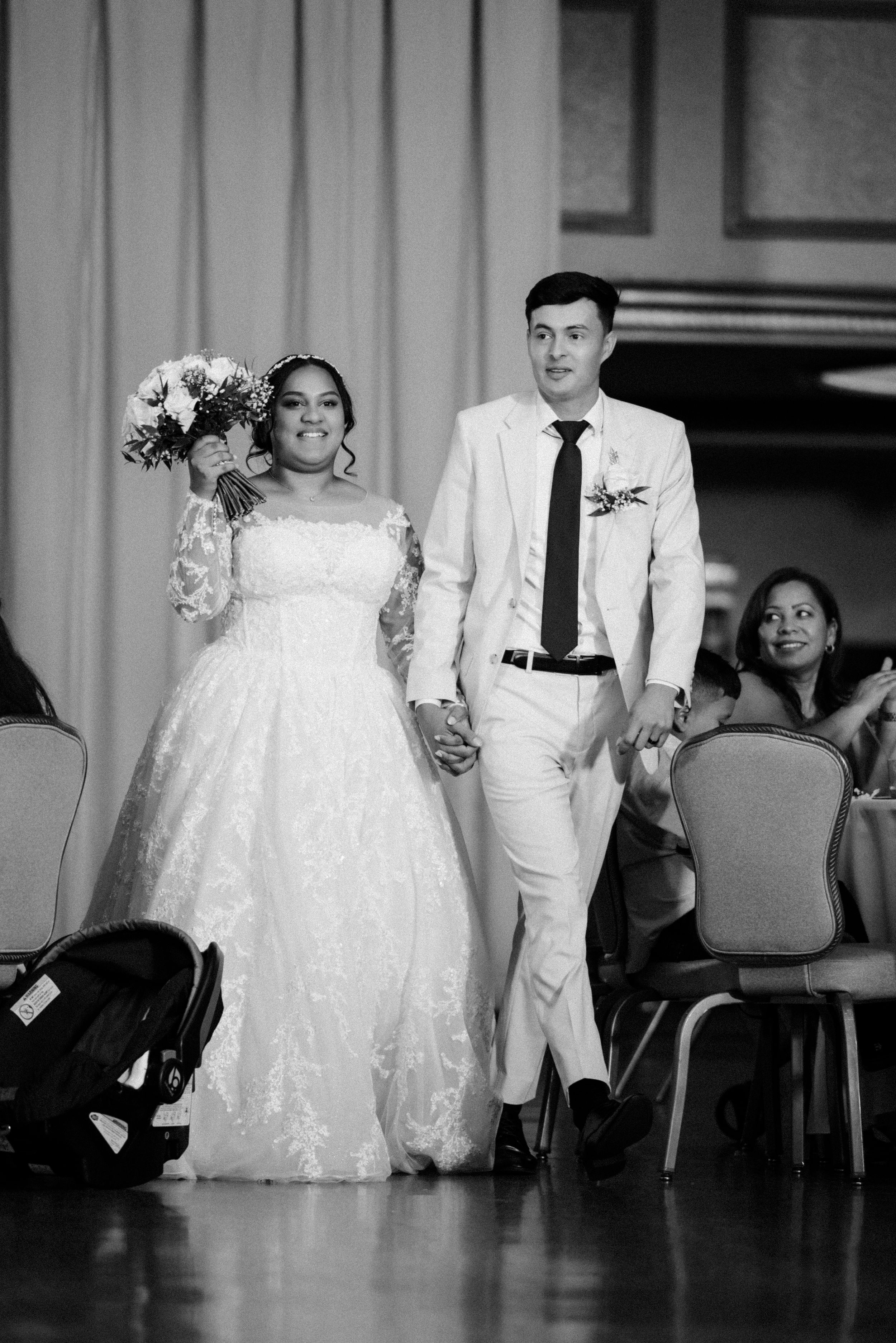 A black and white wedding photo shows a couple walking down the aisle together as guests look on.