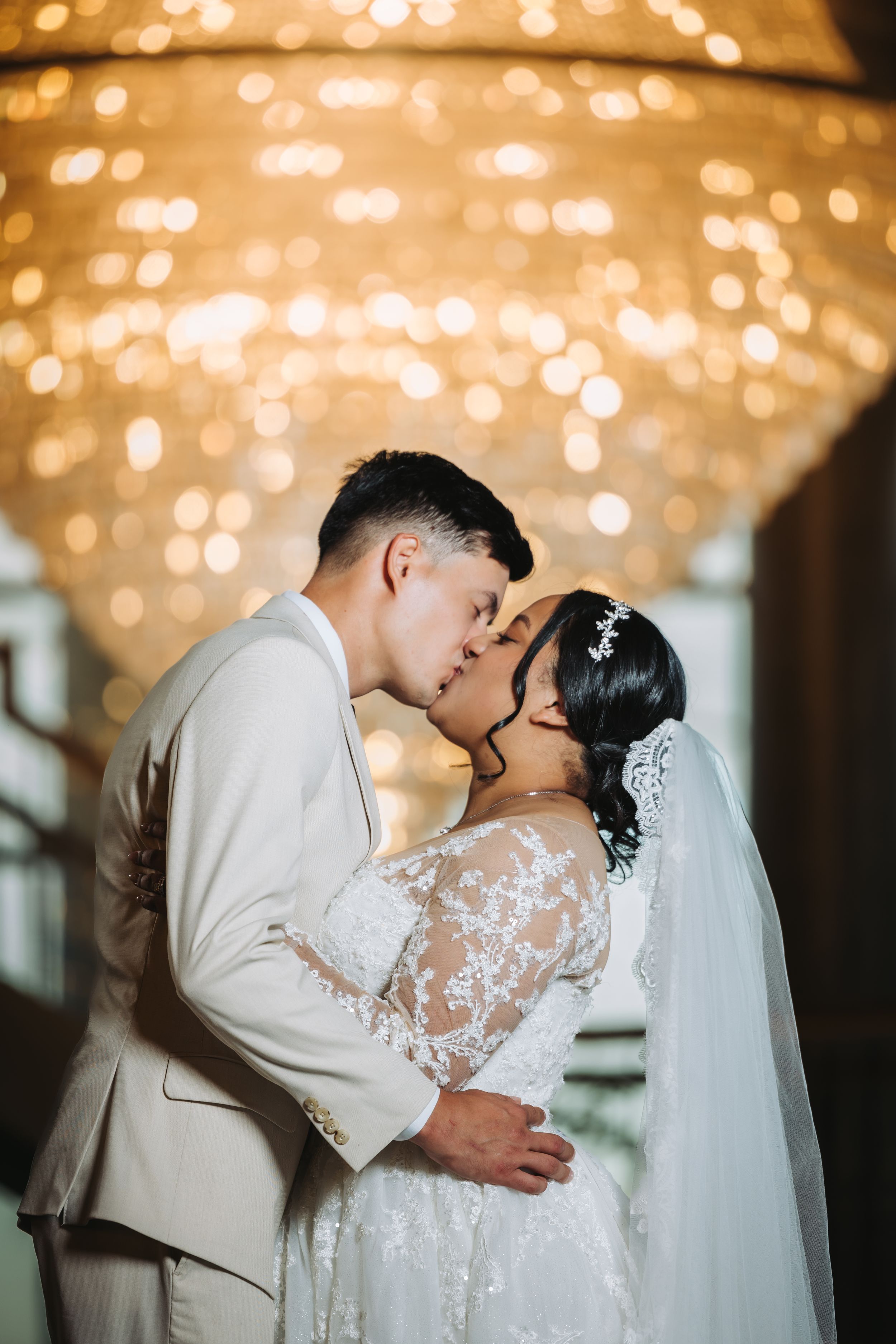 A romantic wedding couple sharing a kiss under warm twinkle lights creating a dreamy, intimate atmosphere.