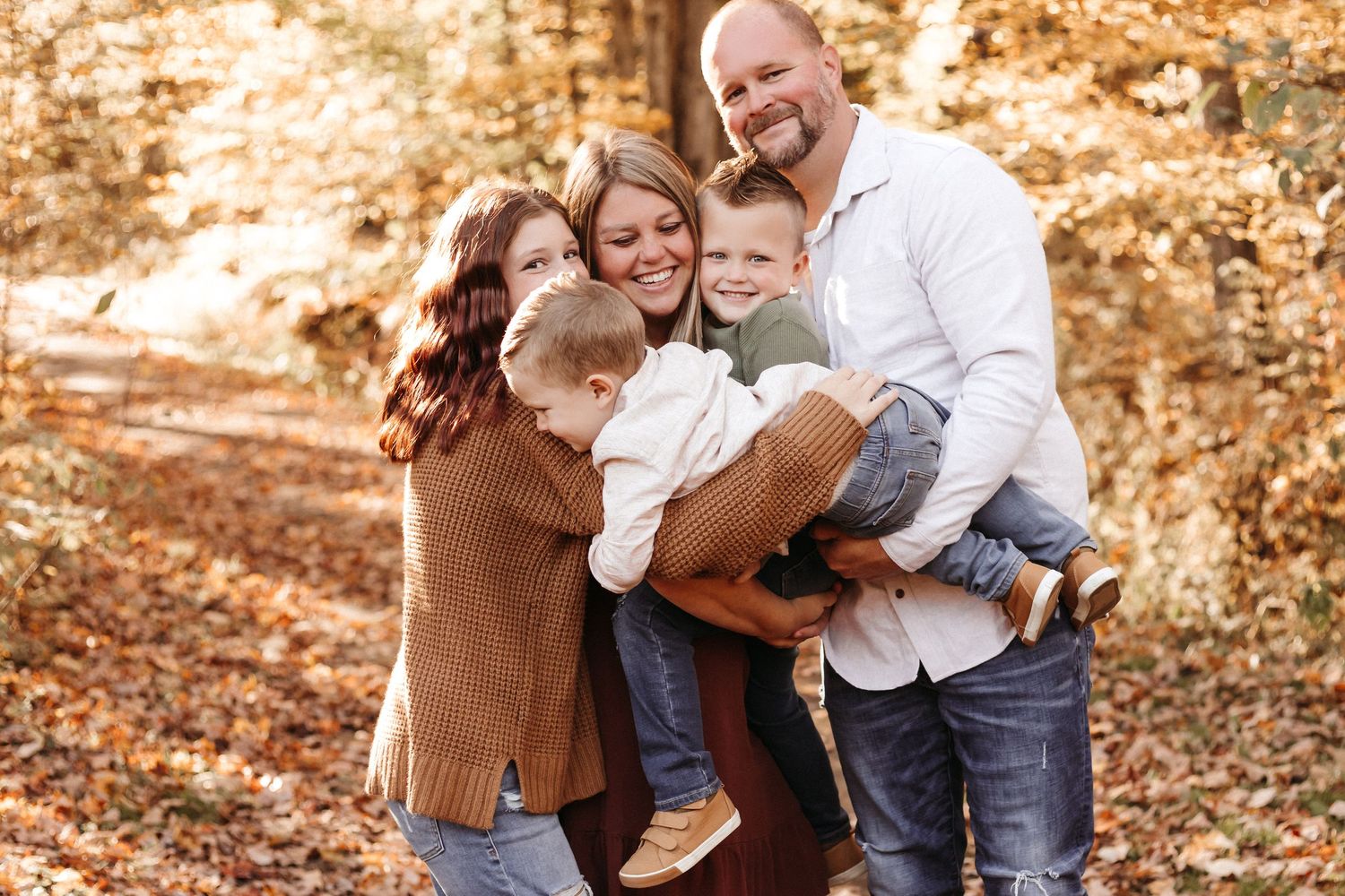 Family embracing and laughing together during fall photo session in woods.