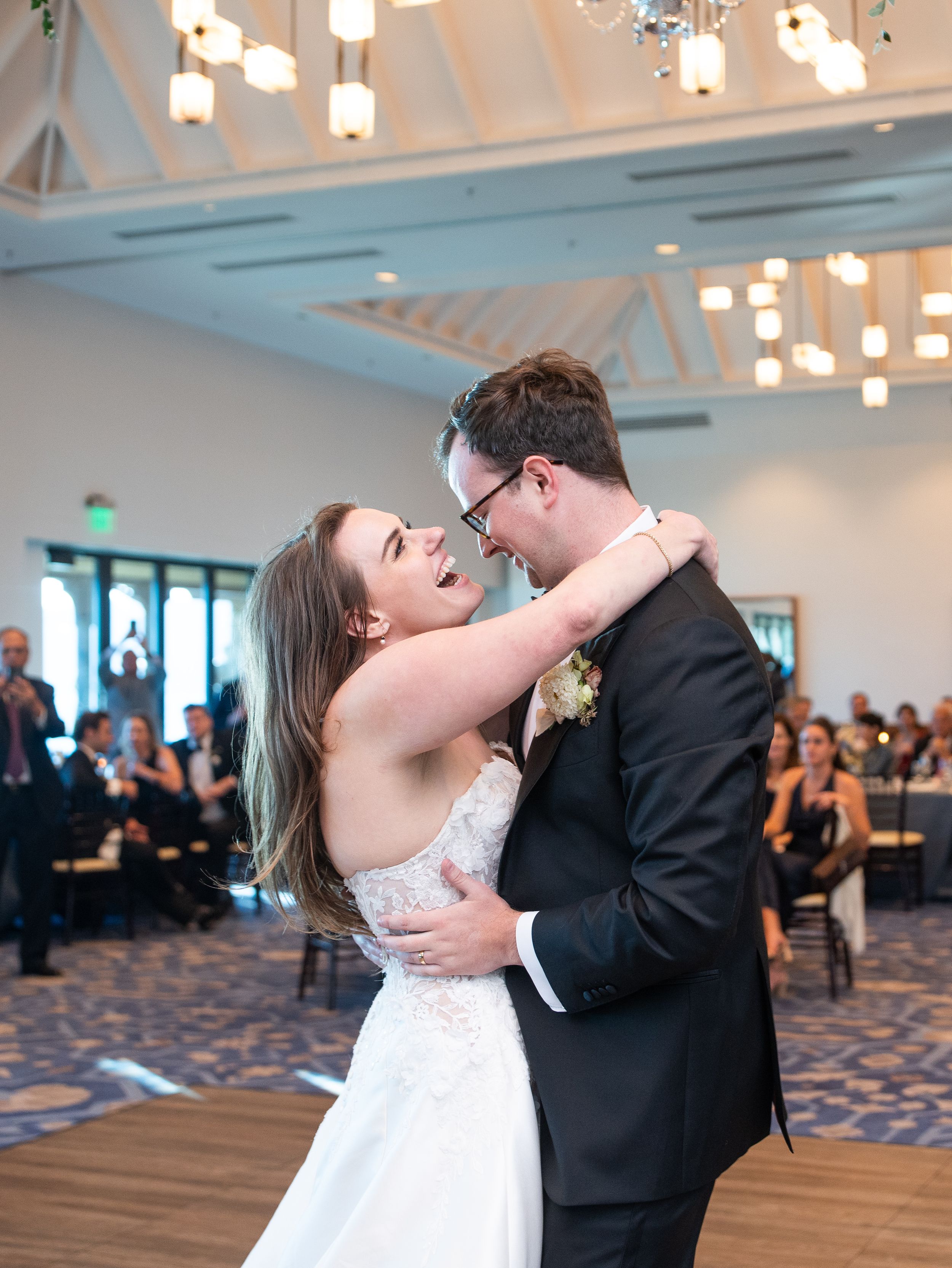 A couple shares a joyful moment during their first dance at a wedding reception in an elegant Hyatt Tahoe ballroom with hanging lights.