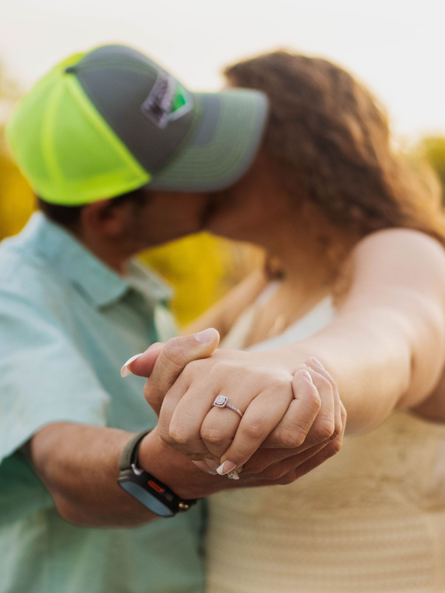 Close-up of hands showing off an engagement ring during a sunny outdoor moment.