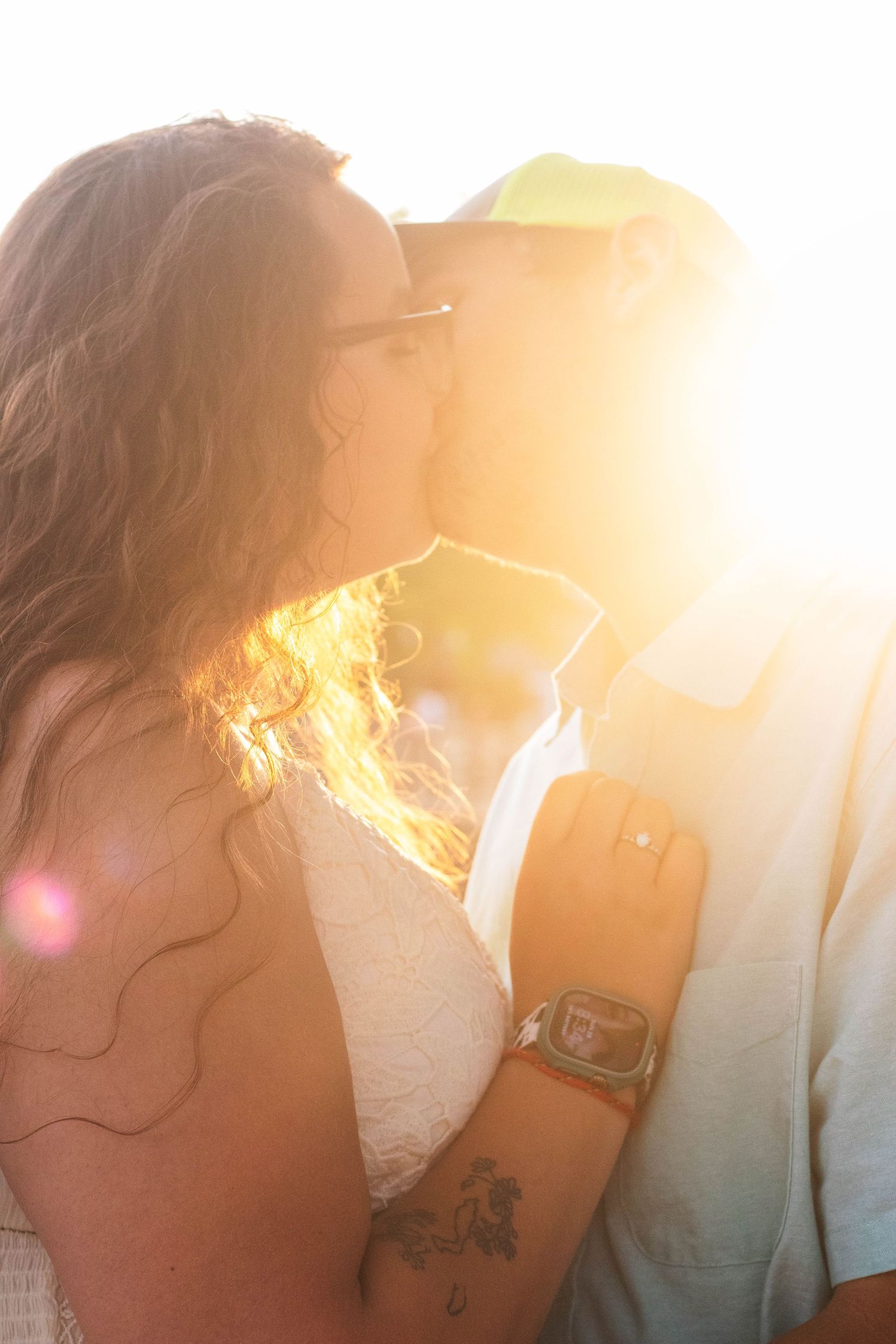 Romantic backlit silhouette of a couple embracing at sunset with golden sunflare illuminating their profiles.