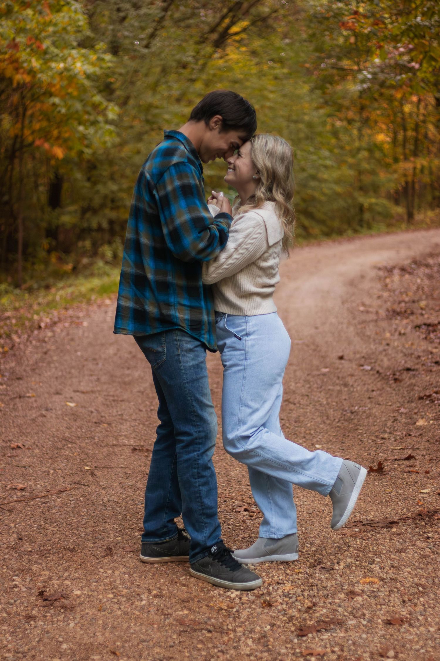 Casual engagement photo of couple in casual attire on autumn forest path.