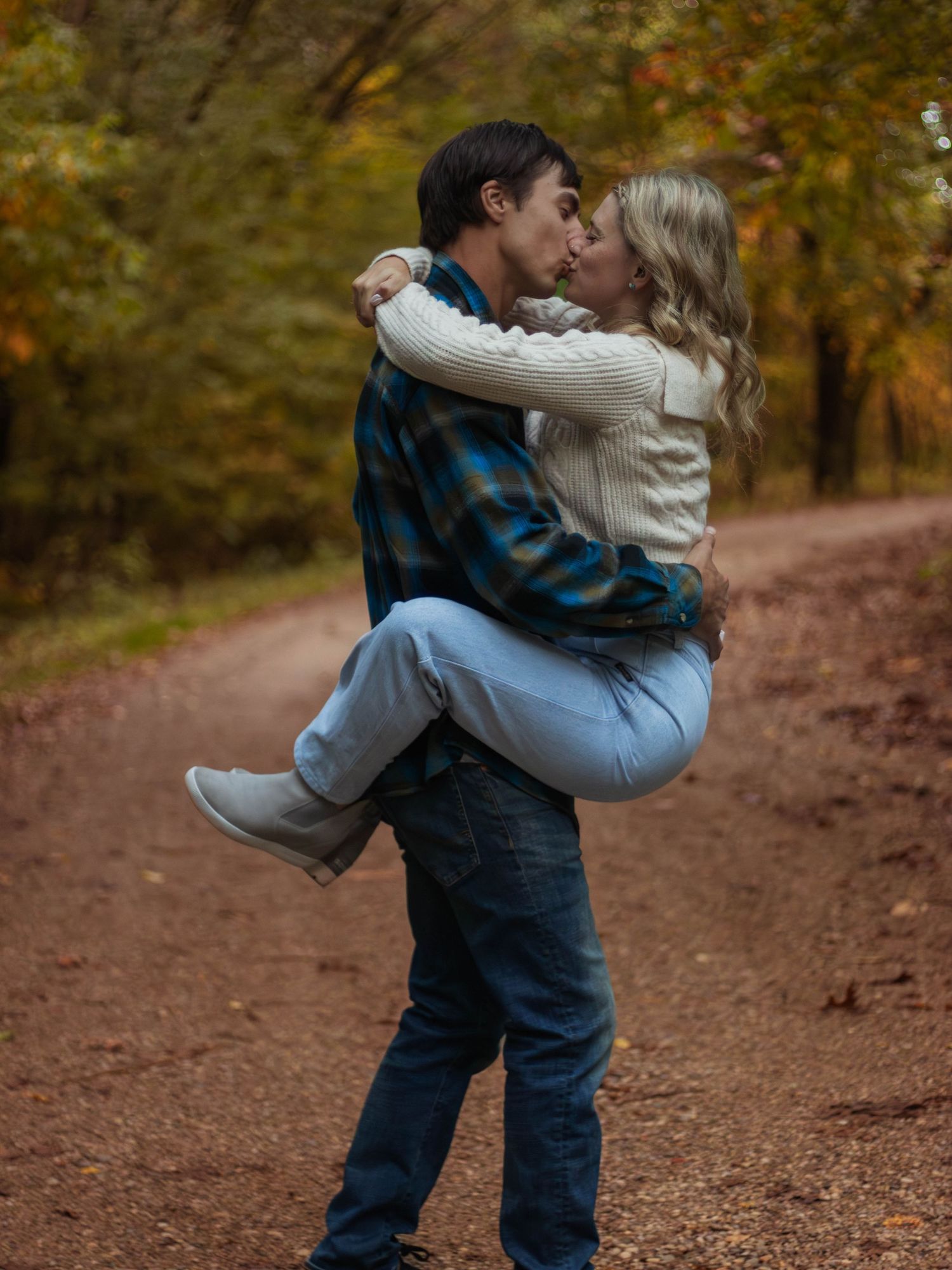 Playful couple embracing on autumn trail with person being carried.