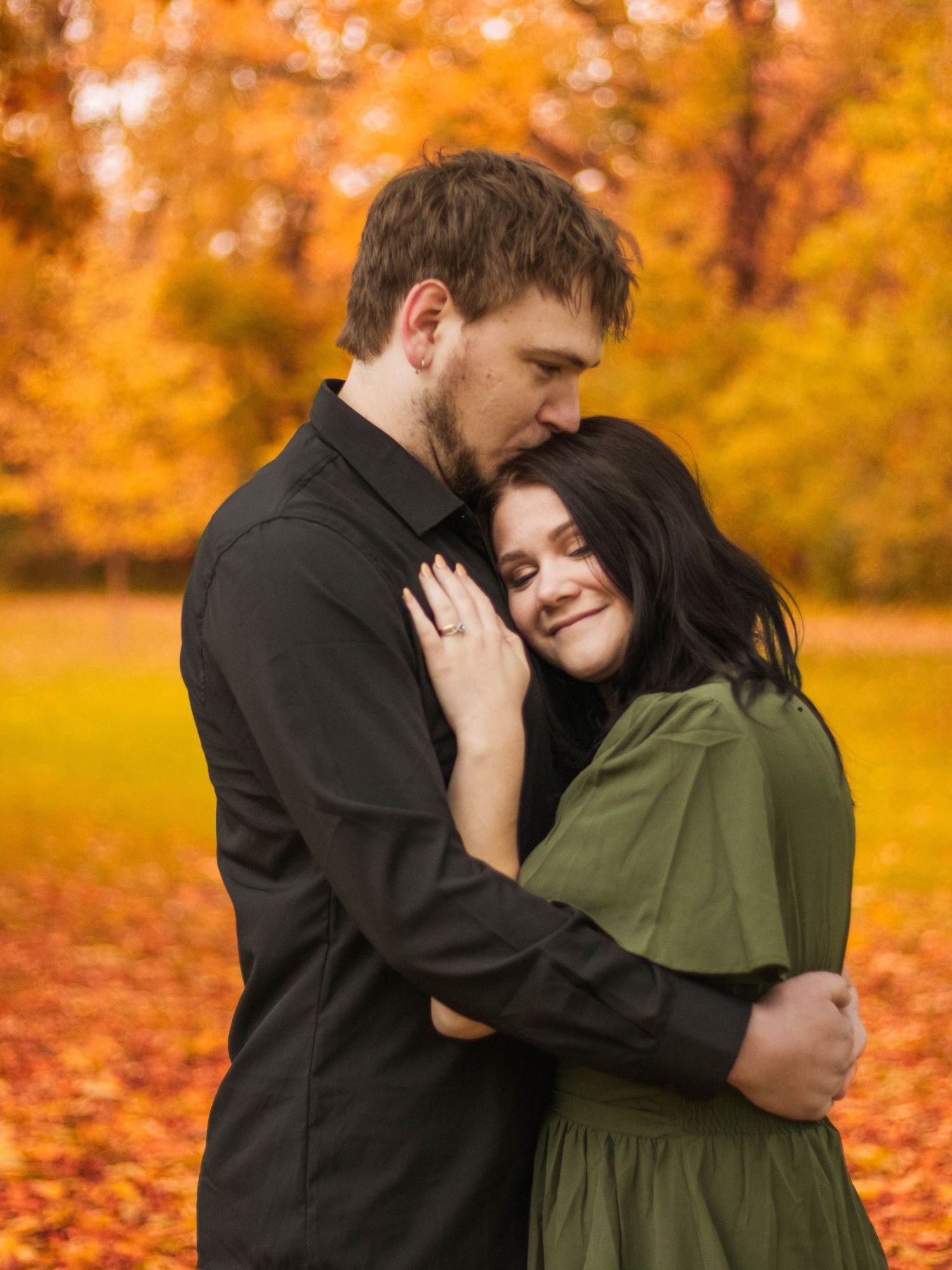 A tender embrace between a couple surrounded by vibrant orange autumn foliage.