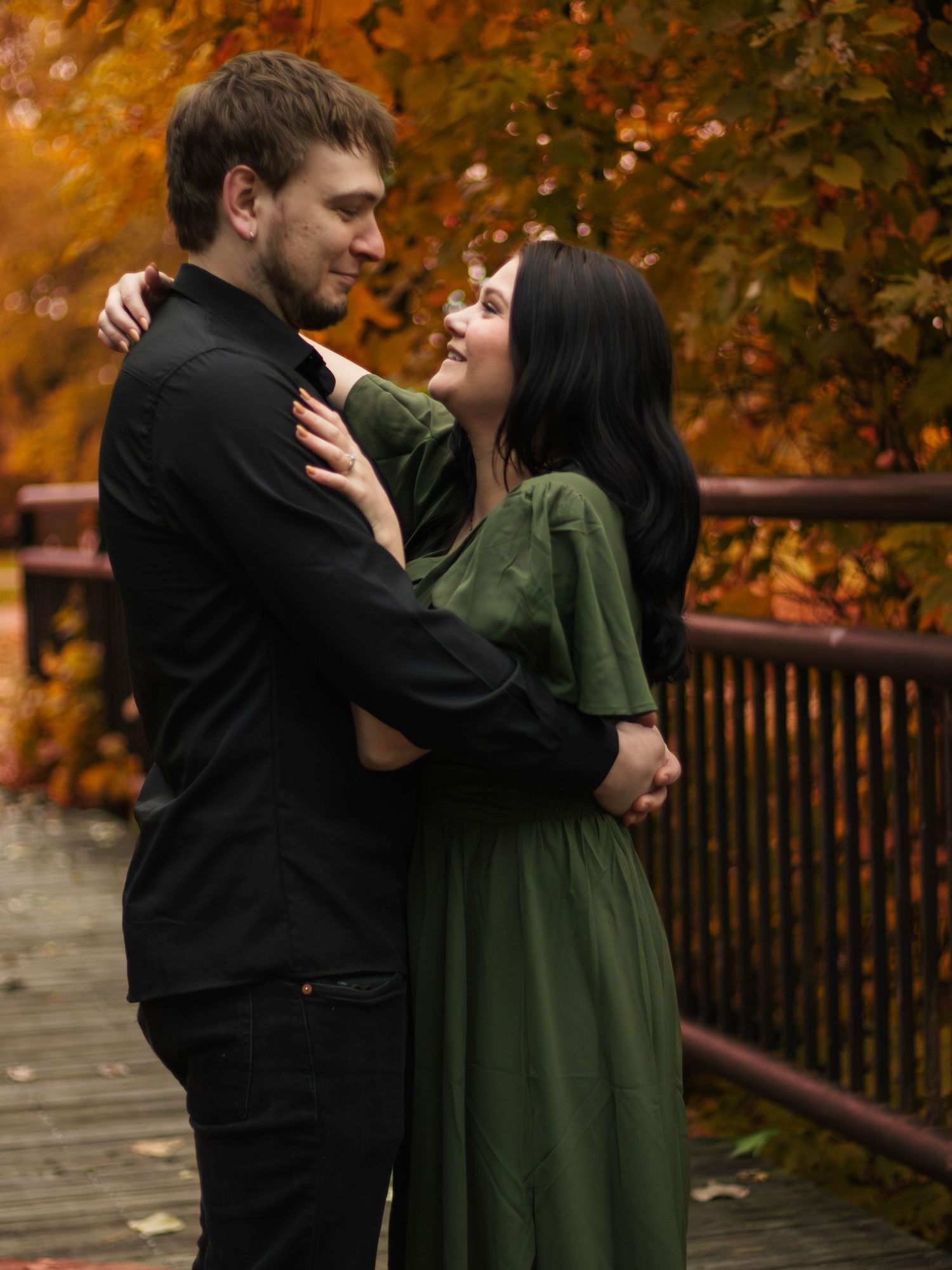 Couple embracing on an autumn boardwalk surrounded by vibrant orange foliage.