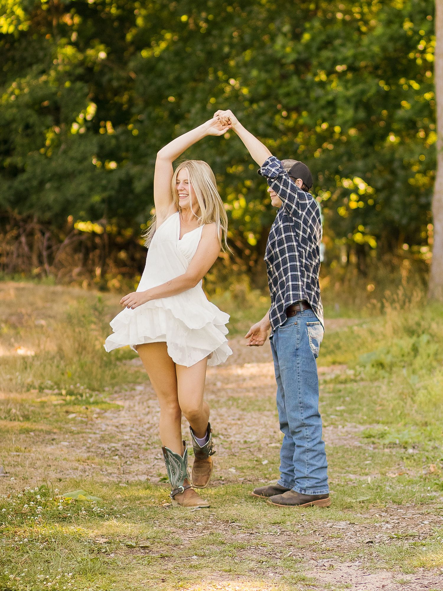 Couple dancing in a field with person in white dress and cowboy boots twirling.