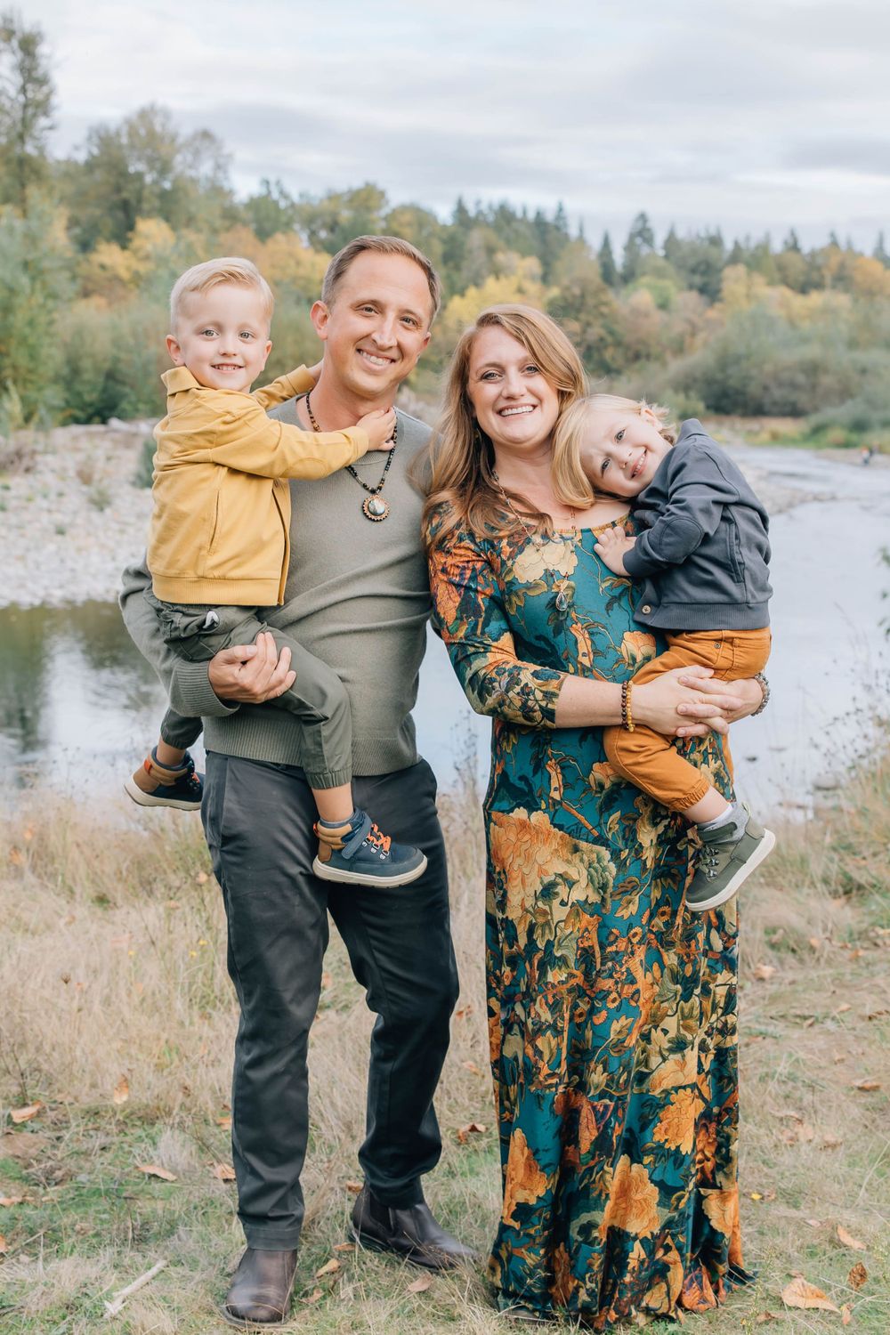 Happy family of four poses near a river surrounded by autumn foliage and trees.