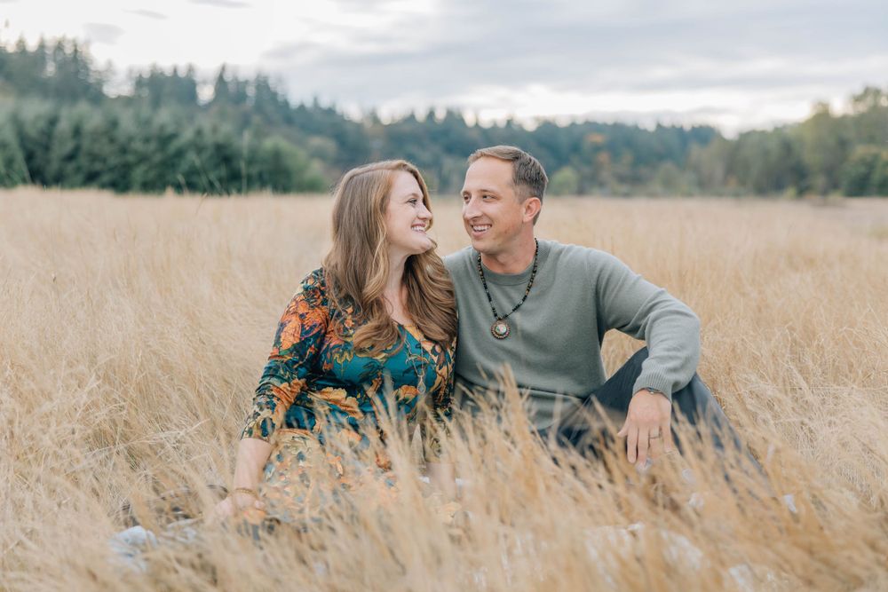 Happy couple sitting together in a golden field of tall grass in autumn.