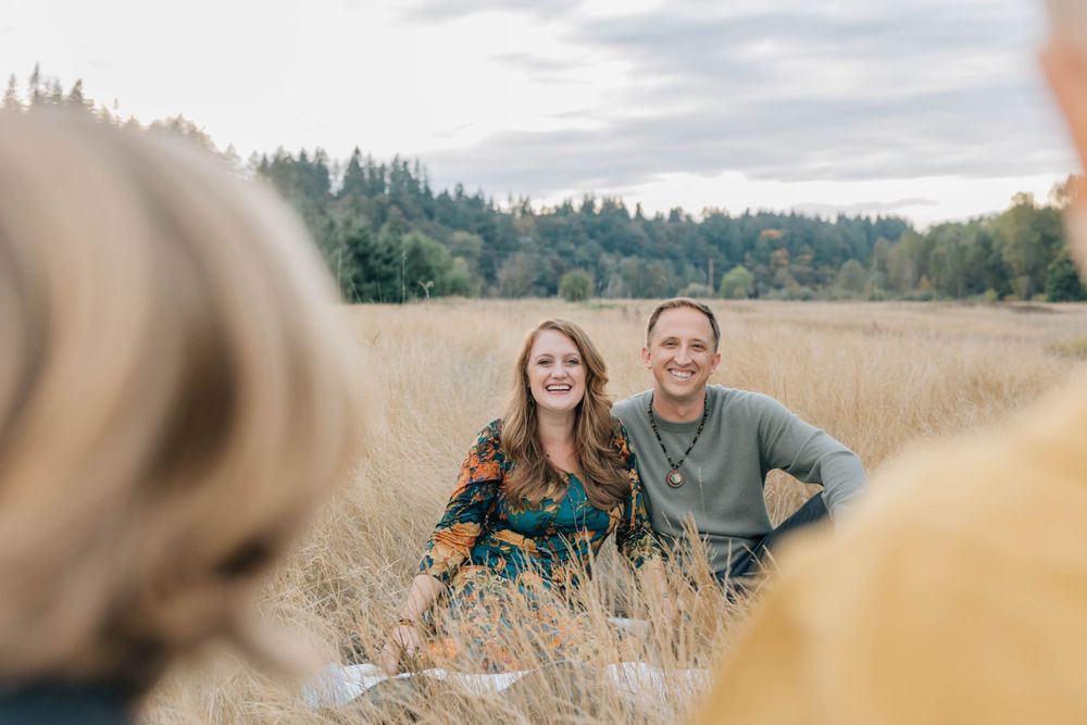 Smiling couple sitting in a golden field with children in the foreground.