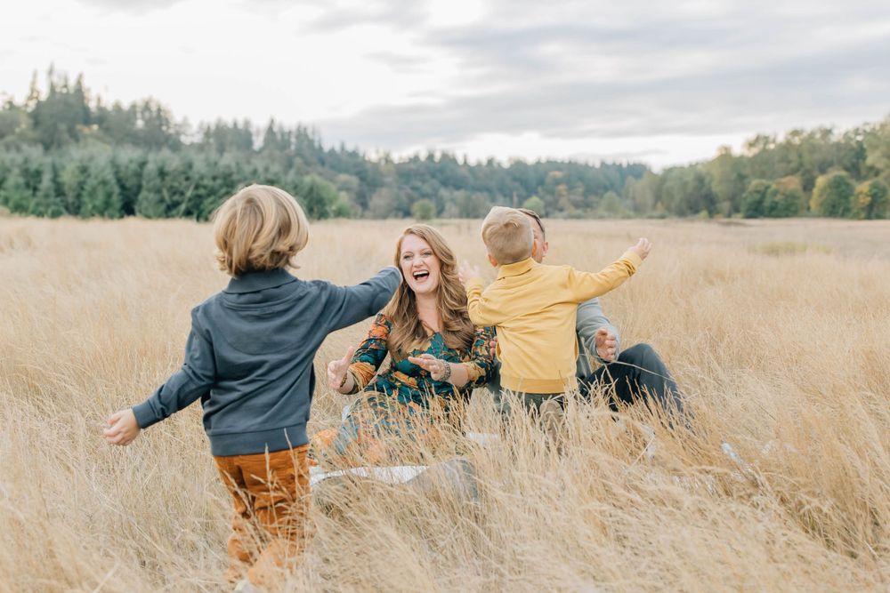 Joyful mother laughing as her two young sons run toward her in a golden field.