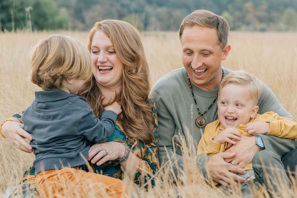 Joyful family of four laughs together while sitting in a golden autumn grass field.