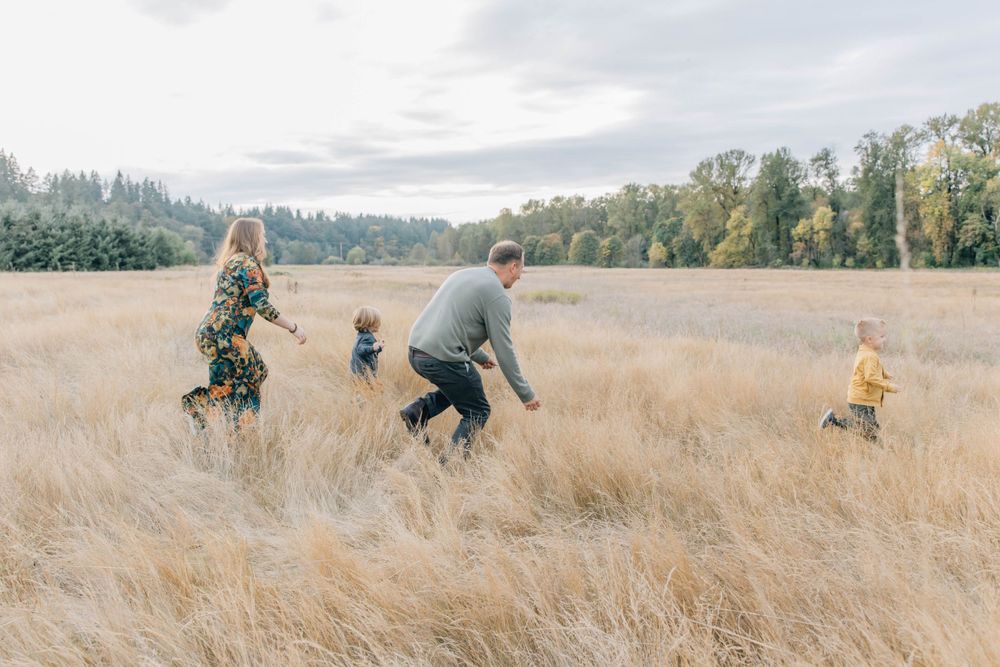 Family of four playing and running together in a golden field on a cloudy day.