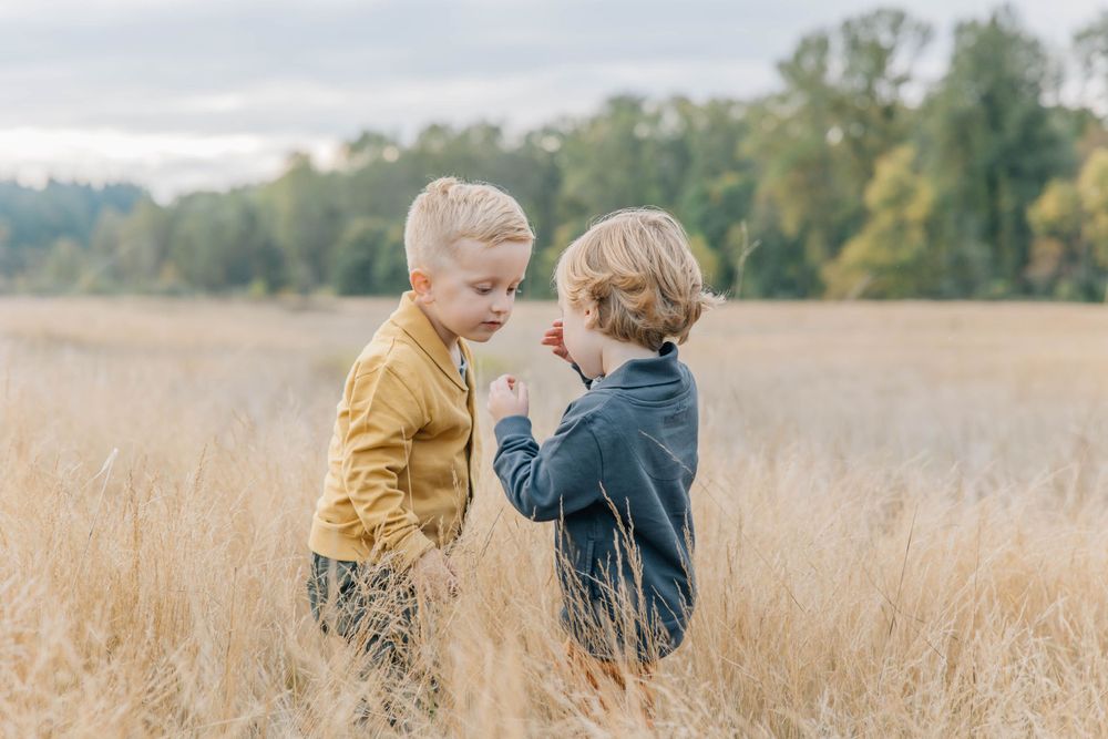 Two young blonde boys interact playfully in a golden field of tall grass during autumn.