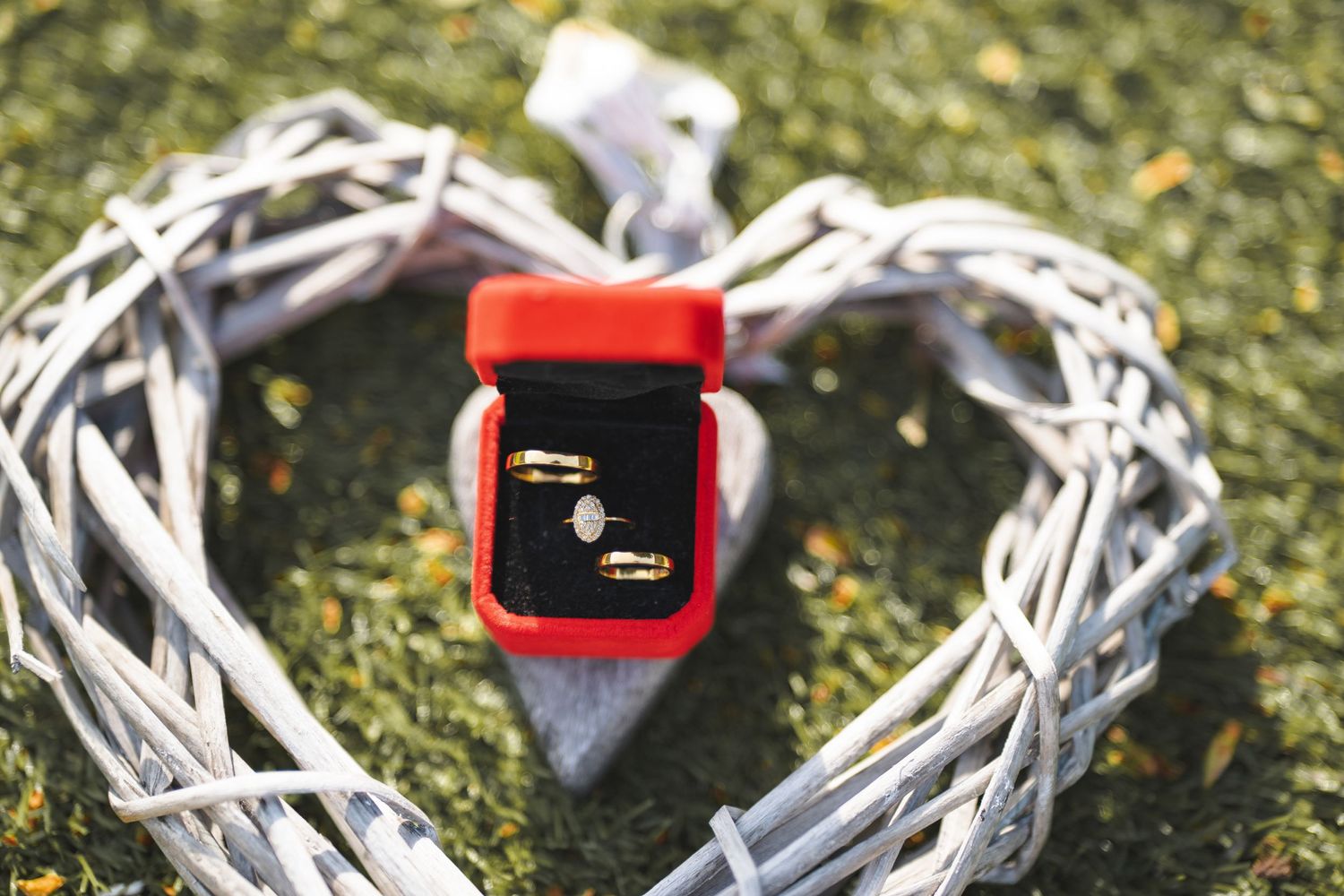 Wedding rings displayed on white decorative woven material with a red ring box.