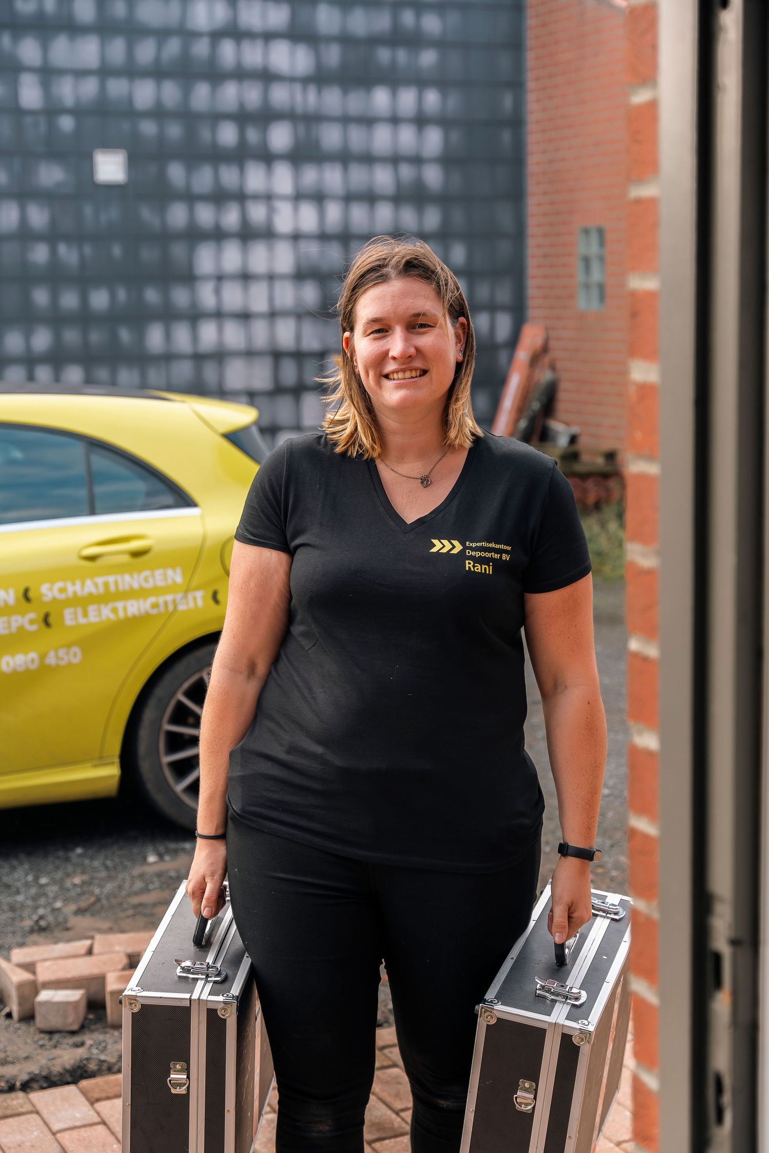 Professional service provider standing with equipment cases next to yellow company vehicle.