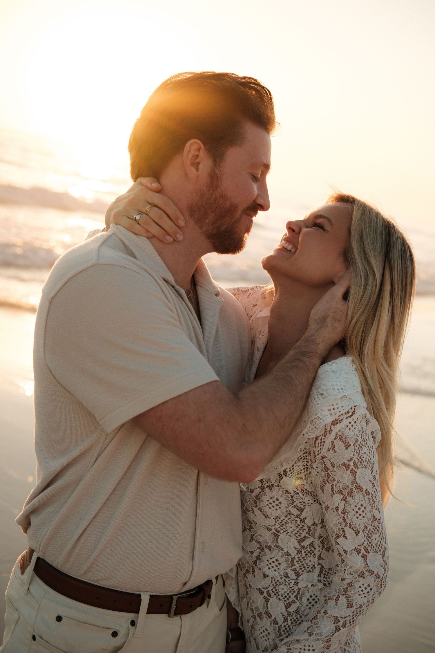 Couple embracing romantically on a beach at golden sunset, smiling and gazing at each other.