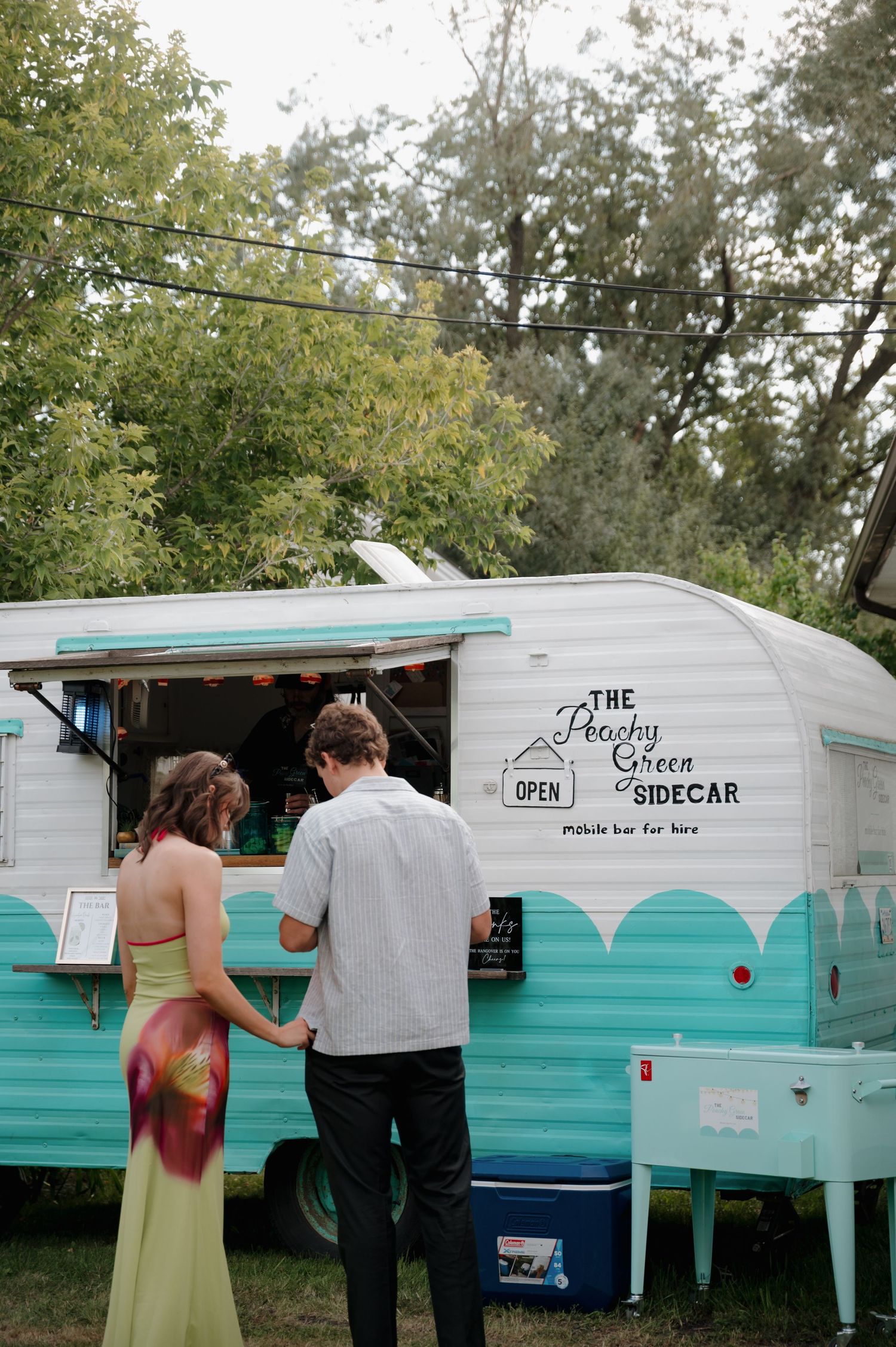 Couple ordering at The Peachy Green Sidecar vintage turquoise mobile pickle bar at outdoor event.