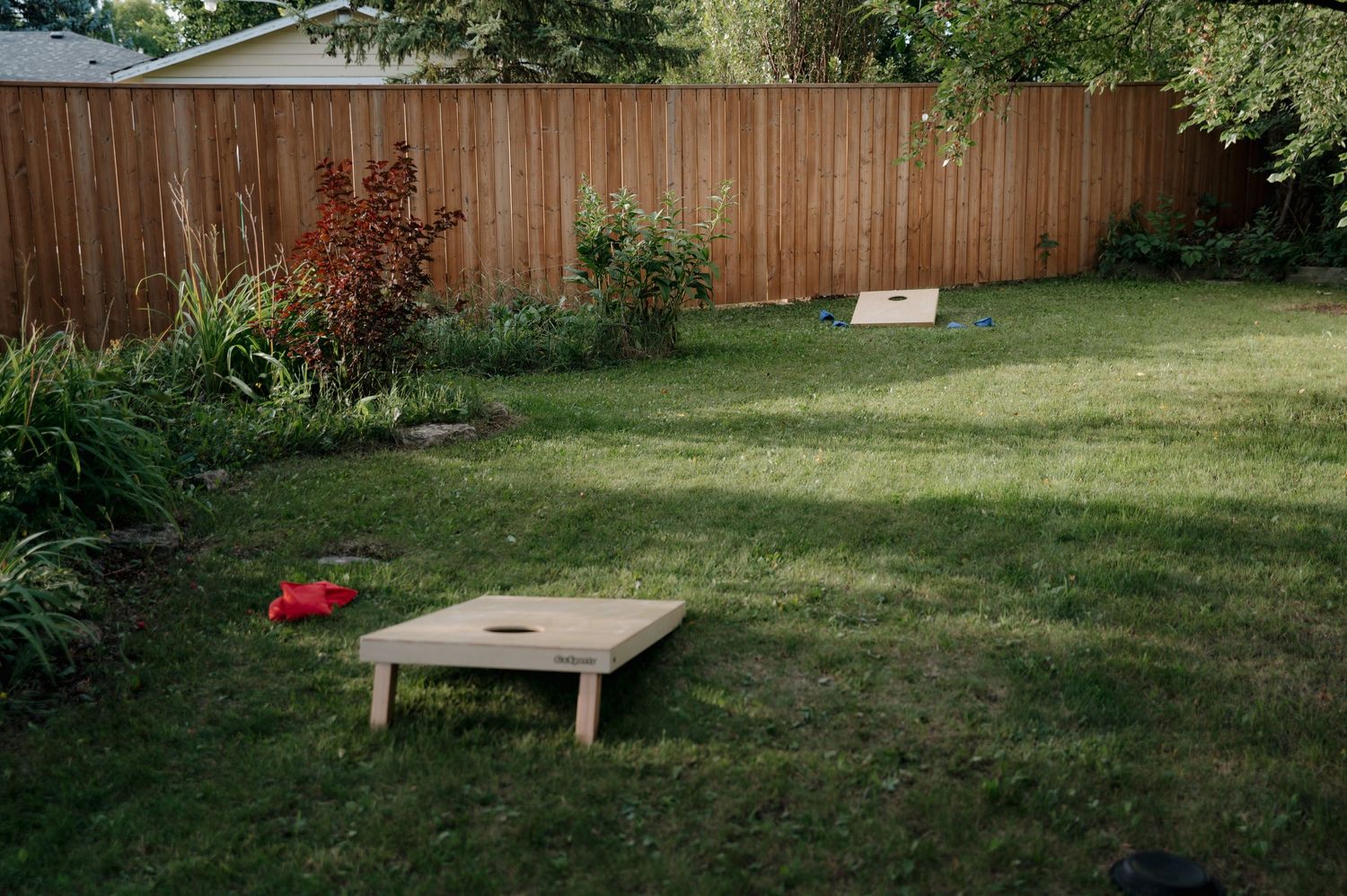 Cornhole lawn game set up in a backyard with wooden boards and red bean bags on green grass.
