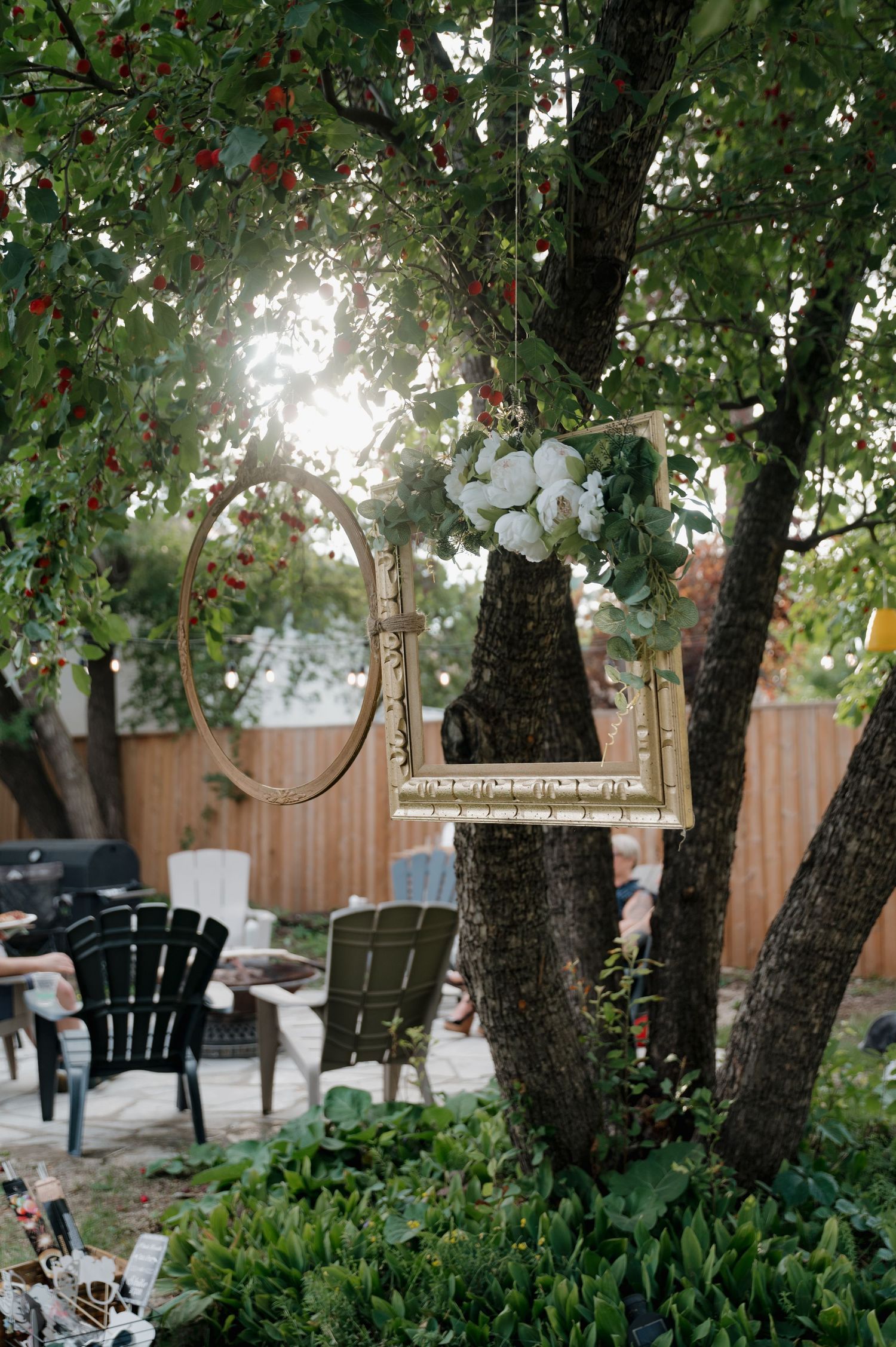Decorative gold frame and floral hoop with white roses hanging from a tree at an outdoor wedding.