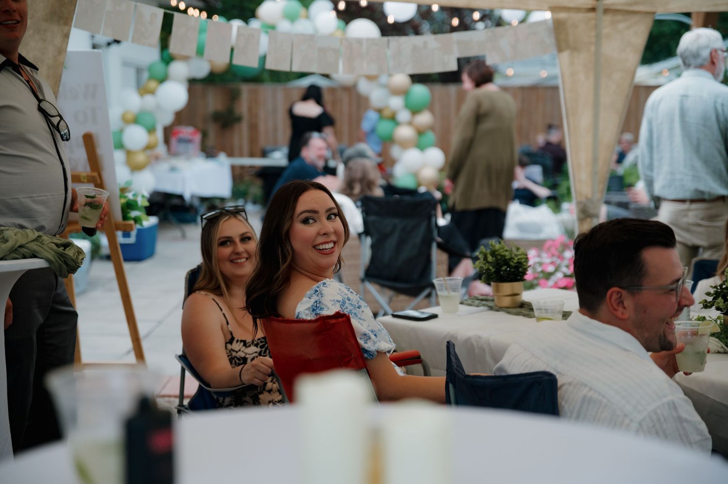 Guests smiling and laughing at a festive outdoor wedding reception under a decorated tent.