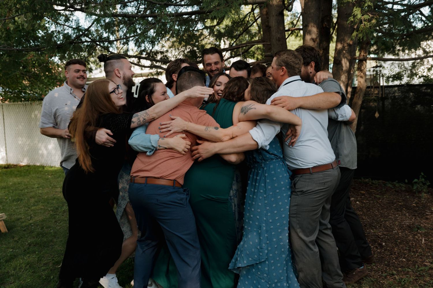 A joyful group of friends sharing a warm group hug outdoors in a backyard setting.