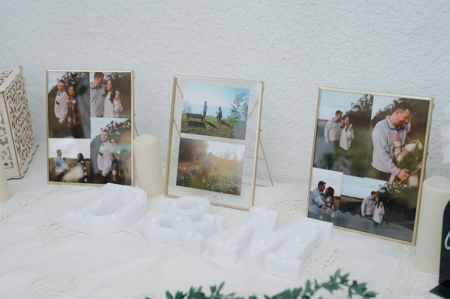 Wedding photo display with framed collages on a white table with candles and decorative letters.