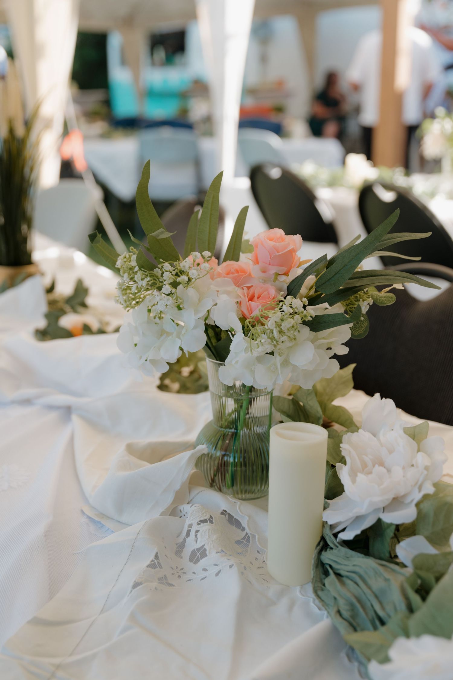 Elegant wedding table centerpiece with pink roses, white peonies, and greenery in glass vase with candle.