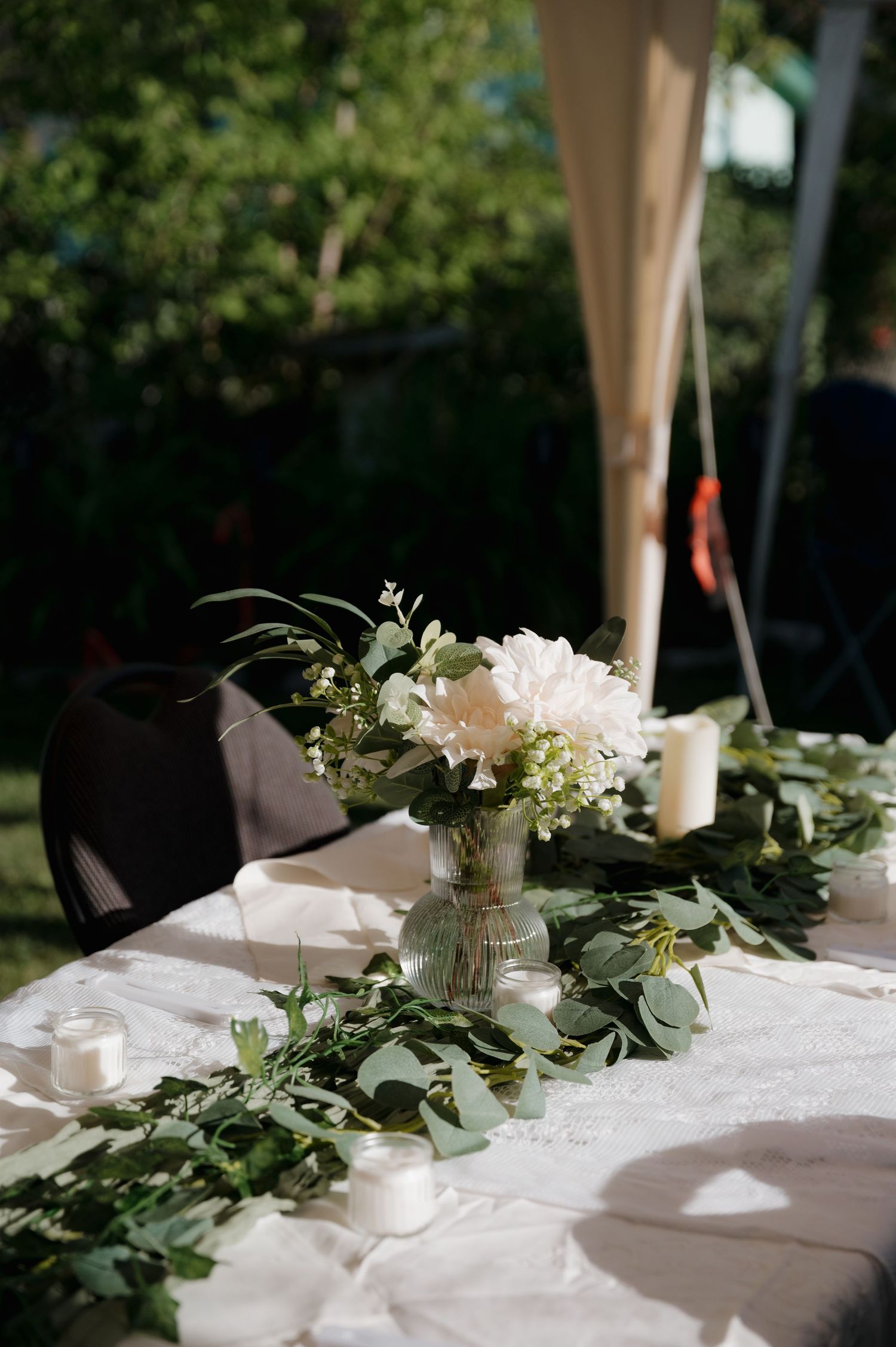 Elegant outdoor wedding table with white floral centerpiece and eucalyptus garland runner.