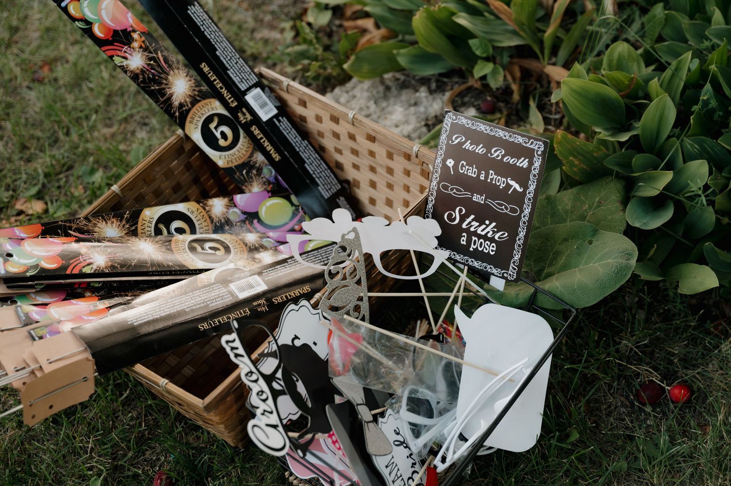 A wicker basket filled with wedding photo booth props and accessories on grass.