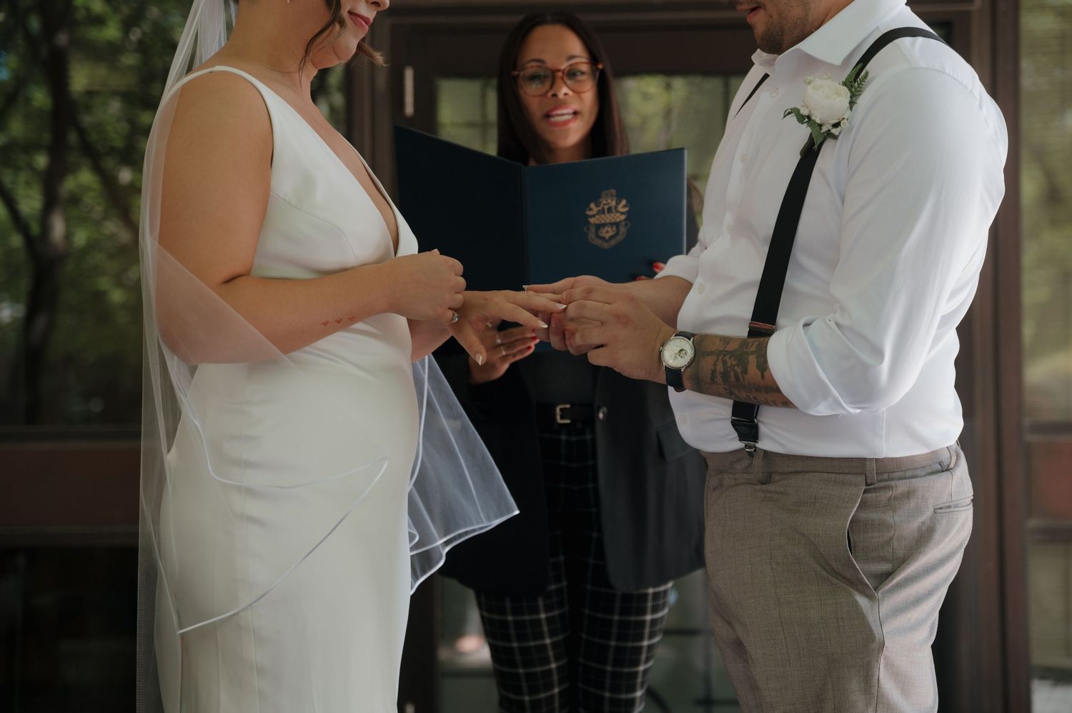 Groom placing wedding ring on brides finger during ring exchange ceremony.
