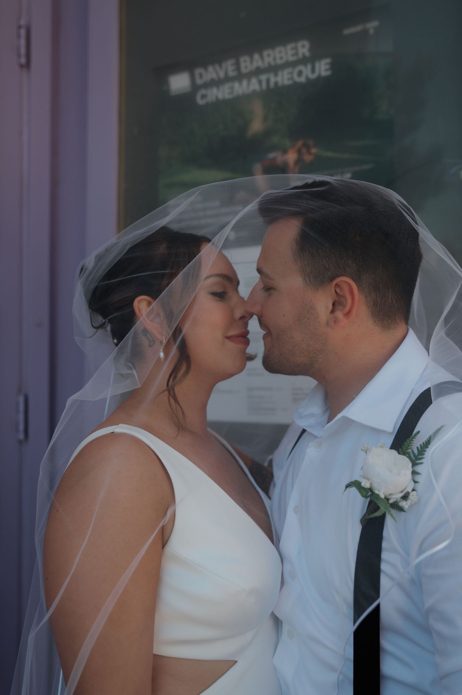 Bride and groom sharing romantic moment under veil outside Dave Barber Cinematheque.