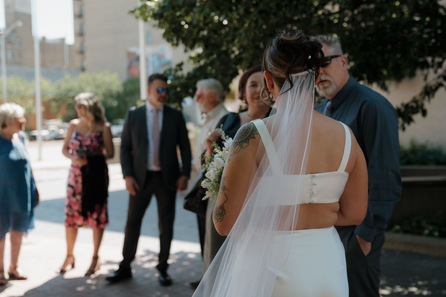 Bride embracing a guest outdoors while family members stand nearby at wedding ceremony.