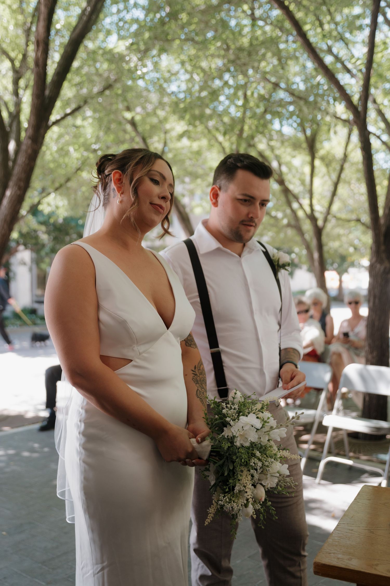 Bride holding white floral bouquet standing with groom during outdoor wedding ceremony.